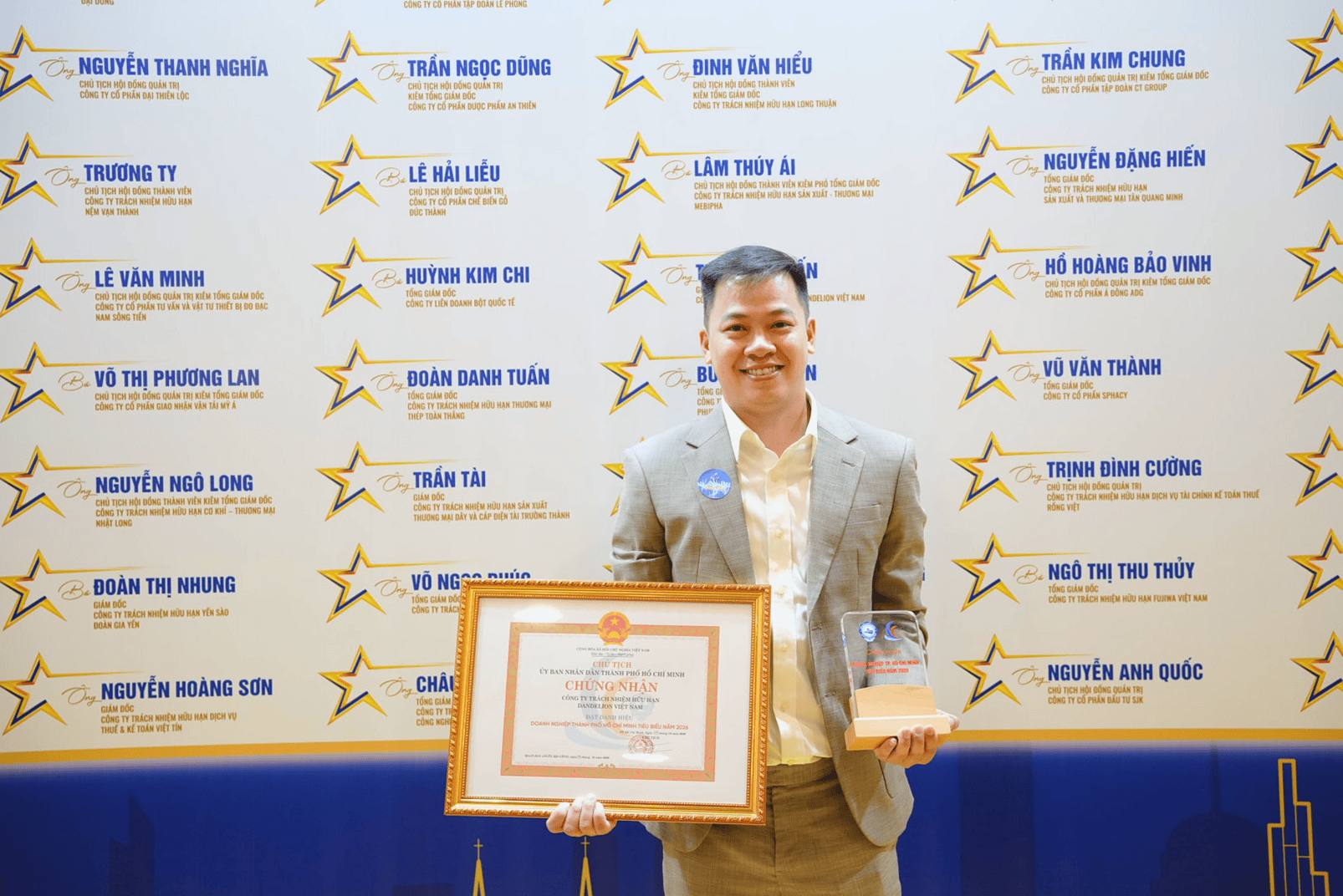Ông Trần Thiên Ấn cầm chứng nhận doanh nghiệp tiêu biểu cùng cúp lưu niệm bên bảng vinh danh